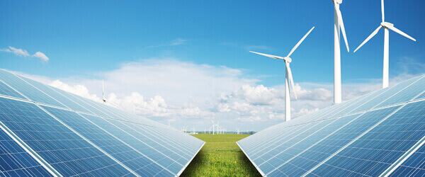 An array of solar panels in the foreground. Three wind turbines in the background. A blue sky with some white clouds