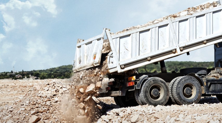 A dump truck unloads rubble and rocks at a construction site