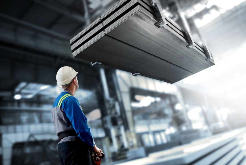 An employee in work clothes is overseeing the transport of large durostat steel plates in a production hall