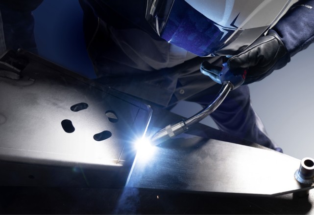 A skilled worker welding a durostat metal component, wearing a safety helmet and holding a welding torch