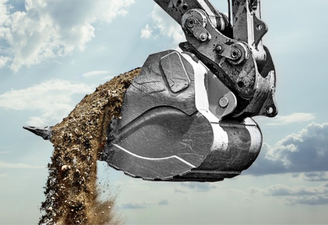 Close-up of an excavator bucket made of durostat steel, lifting a large amount of debris and rocks
