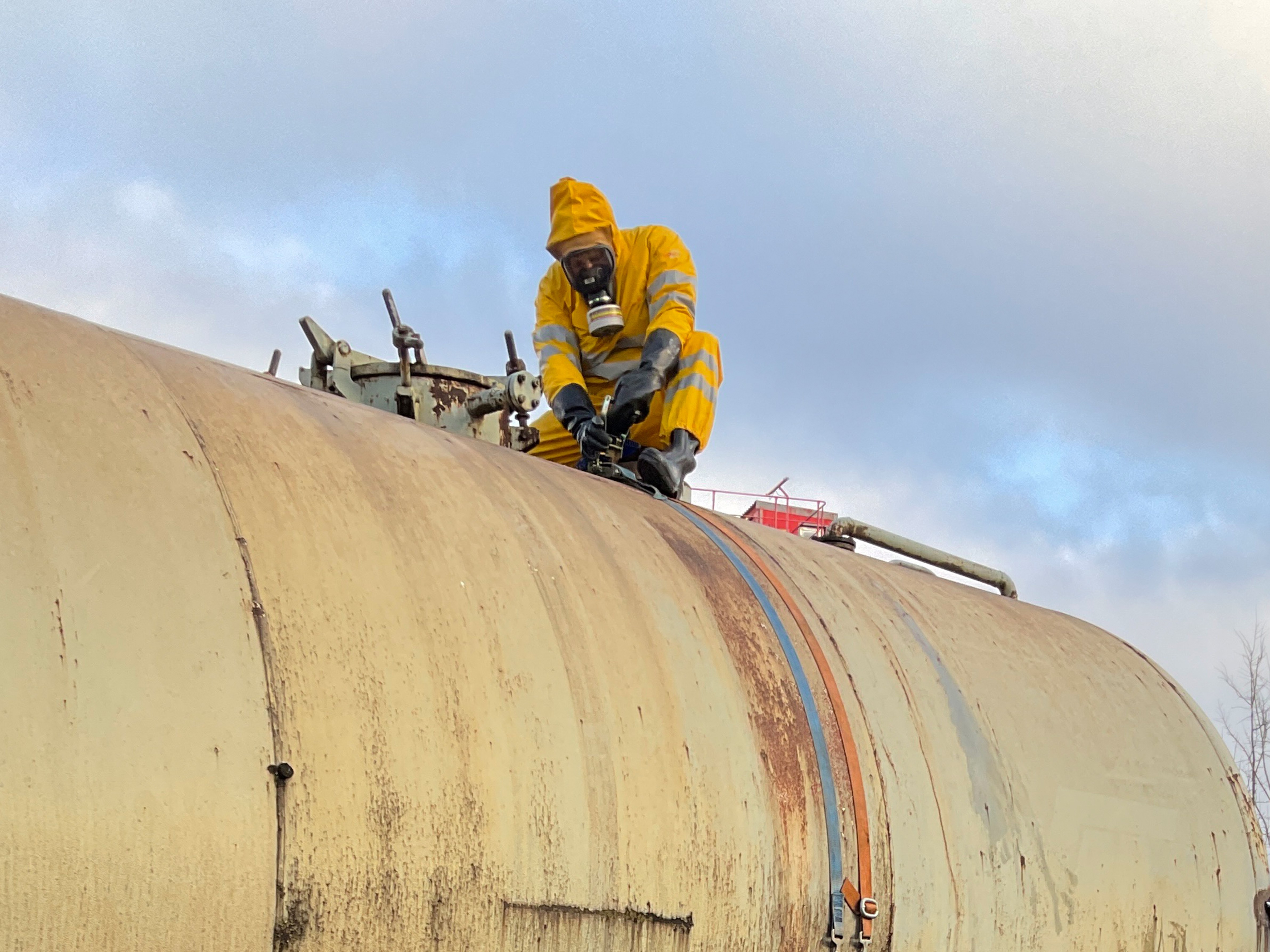 Einsatzkraft in Chemikalienschutzanzug bei Arbeiten an einem Tankbehälter.