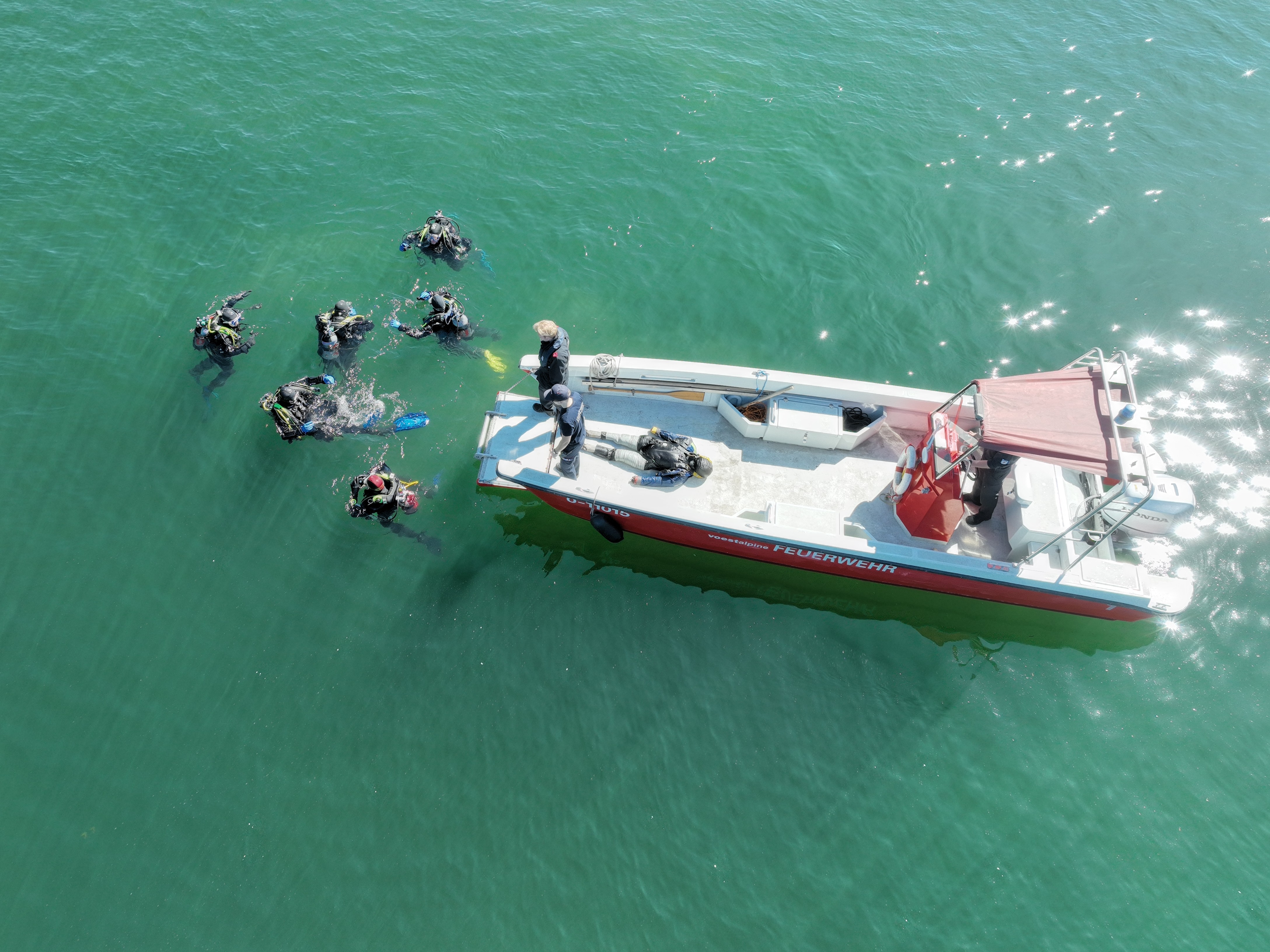 Feuerwehrtaucher bei einer Übung neben einem Einsatzboot auf einem Gewässer.