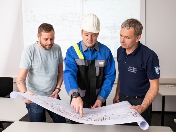 Drei Mitarbeitende besprechen einen Brandschutzplan für eine Industrieanlage.