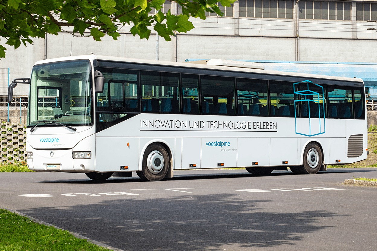 Der weiße Werkstour Bus steht auf dem Parkplatz unter einem Baum.
